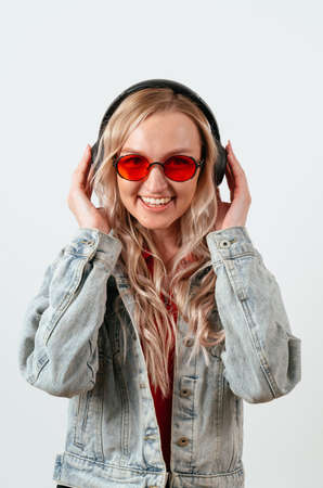 Blonde in headphones on a white background. She is wearing a denim jacket and red glasses.の写真素材
