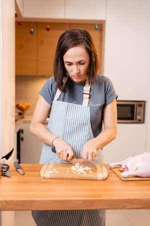 A woman in the kitchen is chopping garlic on a cutting board. Cooking delicious duck for the holiday.の写真素材