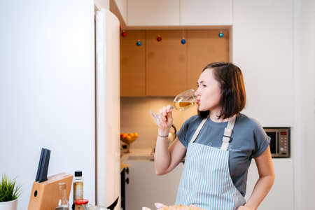 Happy woman with a glass of white wine in the kitchen.