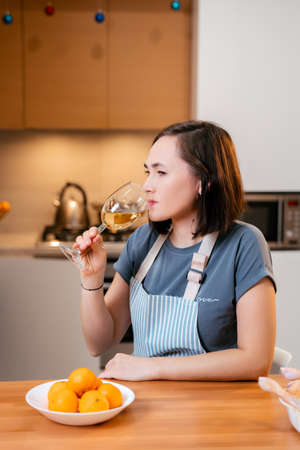 Happy woman with a glass of white wine in the kitchen.の写真素材