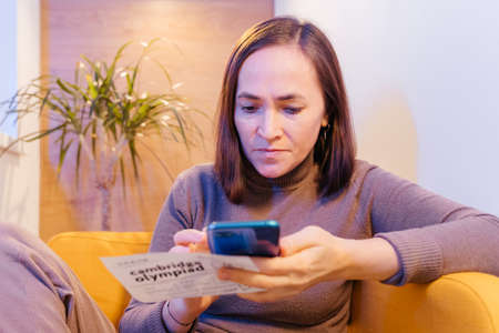A woman is resting in a cozy soft chair with a smartphone. Pretty smiling woman is looking at the...