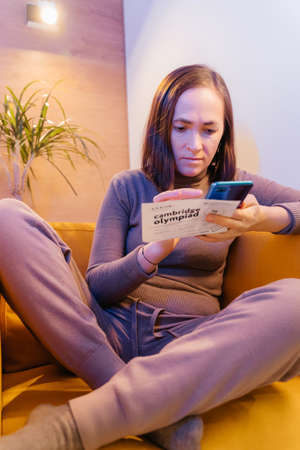 A woman is resting in a cozy soft chair with a smartphone. Pretty smiling woman is looking at the screen of the device, and is typing. Social media funの写真素材