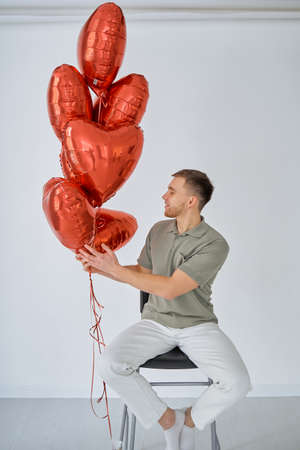 Young man with red balloons. The guy is sitting on a high chair. Celebration of Saint Valentines Dayの写真素材