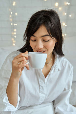Portrait of a brunette girl with a cup of tea on the bed.の写真素材