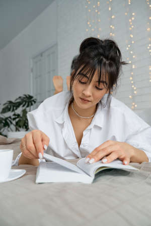 Portrait of a happy beautiful woman reading a book, enjoying her vacation. Young female student studying with book in holiday morning break on bed at home.の写真素材