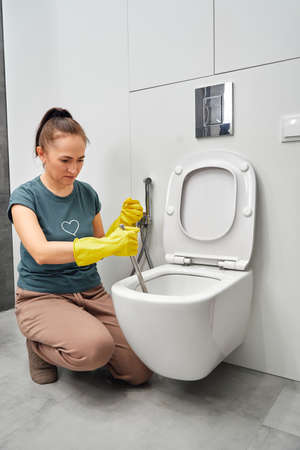 A woman in yellow gloves cleans the toilet bowl with a brush and detergent, the concept of house cleaning and household chores.の写真素材
