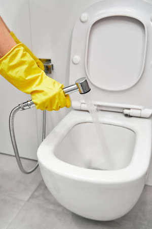Hygienic shower in a female hand, close-up on the background of the toilet. Womens hands in yellow rubber gloves on the background of the toilet.の写真素材