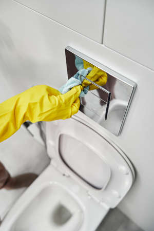 Womens hands in yellow rubber gloves wipe the toilet flush button.の写真素材