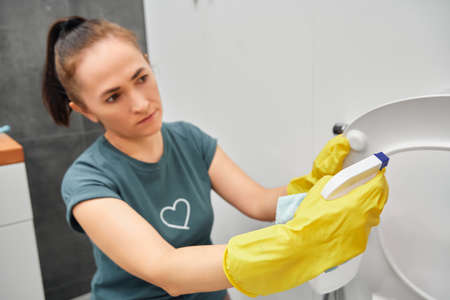 A woman applies a cleaning agent with a sprayer on a toilet seat. Toilet cleaning.の写真素材