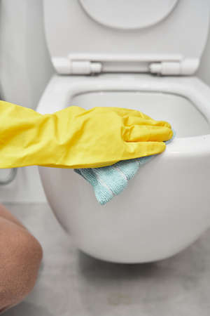 A womans hand in yellow rubber gloves wipes the toilet bowl with a rag.の写真素材