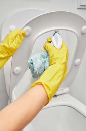 Womens hands in yellow rubber gloves apply a cleaning agent with a sprayer on the toilet seat.の写真素材