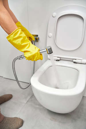 Hygienic shower in a female hand, close-up on the background of the toilet. Womens hands in yellow rubber gloves on the background of the toilet.の写真素材