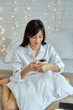 Portrait of a brunette girl with a cup of tea on the bed.の写真素材