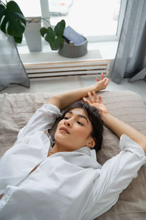 Sexy glamorous brunette in a white shirt is lying on the bed.