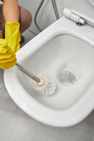 Womans hand in yellow gloves cleans the toilet bowl with a brush and detergent, the concept of house cleaning and household chores.の写真素材