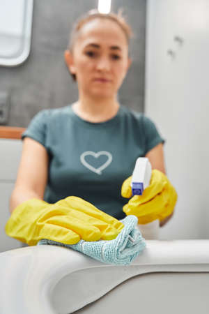 A woman wipes the toilet bowl with a napkin, a rag.の写真素材