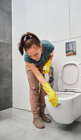 A woman in yellow rubber gloves wipes the toilet bowl with a rag. Toilet cleaning and disinfection.の写真素材