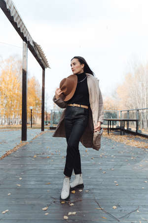 The girl holds a hat in her hand on her chest. Autumn portrait of a girl in a beige coat and hat.の写真素材