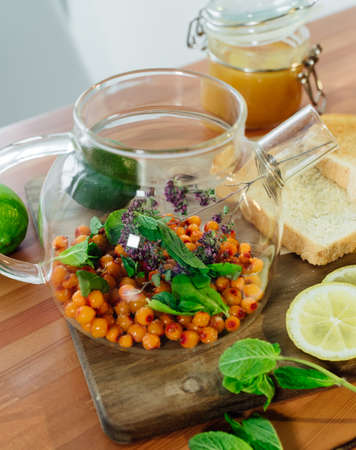 Beautiful glass teapot with sea buckthorn berries, dried thyme and green mint leaves.の写真素材