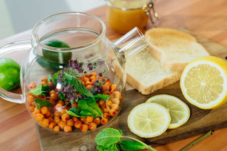 Beautiful glass teapot with sea buckthorn berries, dried thyme and green mint leaves.の写真素材