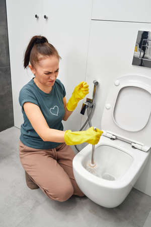 A woman in yellow gloves cleans the toilet bowl with a brush and detergent, the concept of house cleaning and household chores.の写真素材