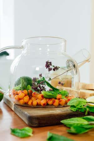 Beautiful glass teapot with sea buckthorn berries, dried thyme and green mint leaves.の写真素材