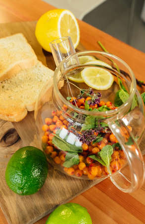 Beautiful glass teapot with sea buckthorn berries, dried thyme and green mint leaves.の写真素材