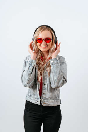 Happy blonde girl in glasses and headphones on a white background.の写真素材