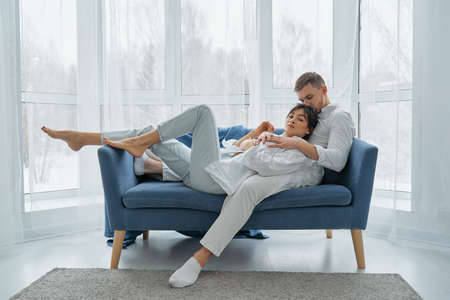 Happy dreamy young caucasian couple rest cuddle on couch in room thinking or visualizing, smiling millennial man and woman relax on sofa at home, hug and embrace.の写真素材
