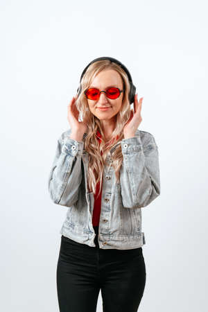 Happy blonde girl in glasses and headphones on a white background.の写真素材