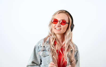 Blonde in headphones on a white background. She is wearing a denim jacket and red glasses.の写真素材
