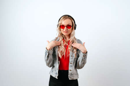 Blonde in red glasses and a denim jacket with a surprised look on a white background, hand gesture.の写真素材