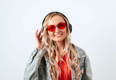Blonde in headphones on a white background. She is wearing a denim jacket and red glasses.の写真素材
