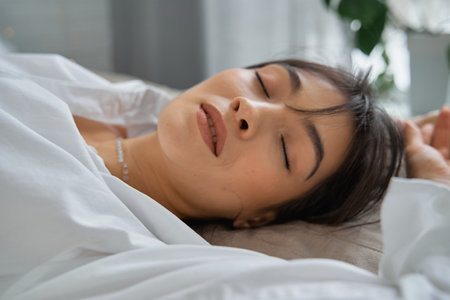 Sexy glamorous brunette in a white shirt is lying on the bed with her eyes closed.の写真素材