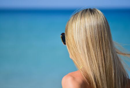 Closeup of blond hair girl looking something in the distance with wind in her hair. Woman body part on the beach - no visible faceの写真素材