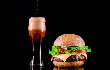 Close-up of delicious fresh home made burger with lettuce, cheese, onion, tomato and cola drink or dark beer with ice on black backgroundの写真素材