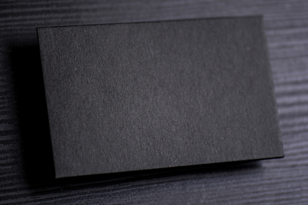Mock up of blank textured black business card on dark wooden background.の写真素材