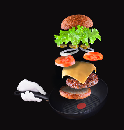 Burger parts flying in air isolated on black. Hand holding Frying pan.の写真素材