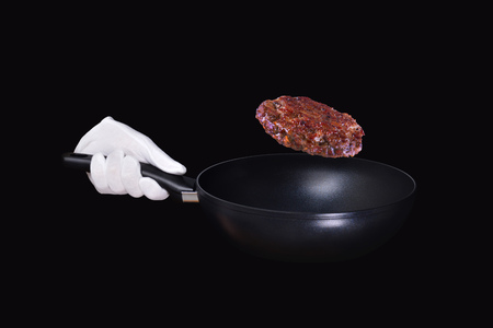 Hand holding Frying pan. White glove holding black pan with fried budger patties in the airi solated on black background.の写真素材