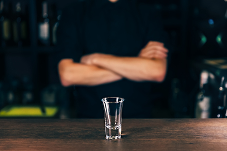 Barmen hand with bottle pouring beverage into glass. Bartender pouring strong alcoholic drink into small glass on bar, shots, on bright background.の写真素材