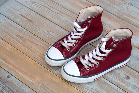 Grunge wooden background with red used vintage canvas sneakersの写真素材