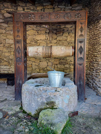 Old wooden and chalk fountain with rusty metal bucket and chain. Rustic style.の写真素材