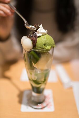 A woman holding a spoon eating the traditional Japanese dessert, a glass of matcha ice creamの写真素材