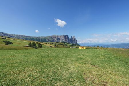 Landscapes on Alpe di Siusi with Schlern Mountain Group in Background and small cabins on the grassland in Summer, South Tyrol, Italyの写真素材
