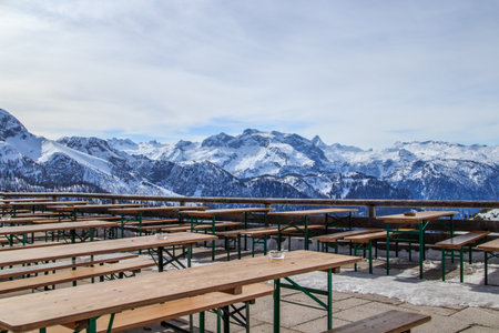 Outdoor restaurant terrace on top of snow mountain, with wooden tables in foreground and Jenner mountain in distance Bavaria, Germanyの写真素材