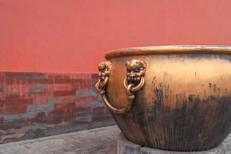 Golden water tank with lion statue against red wall in the Forbidden city