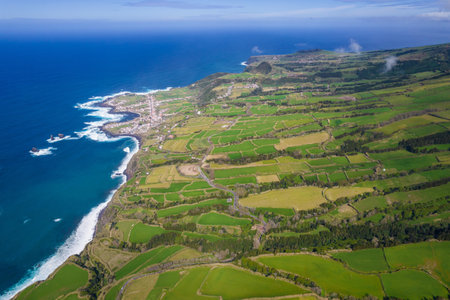 Aerial view of the coastline on Sao Miguel Island, with town buildings, green farmland and volcanic mountains, Azores, Portugalの写真素材