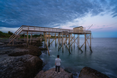 Sunset landscapes at the coastline of Saint-palais-sur-mer, with a man standing on the cliff looking at the traditional carrelets along the sea in Charente-Maritime, Franceの写真素材