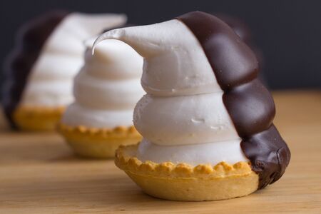 cupcakes in the shape of funny penguins of meringue with chocolate over wood piece on black backgroundの写真素材