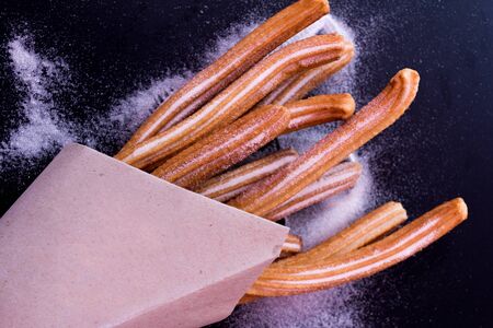 Churros sticks fresh hot with sugar in paper bag on dark backgroundの写真素材
